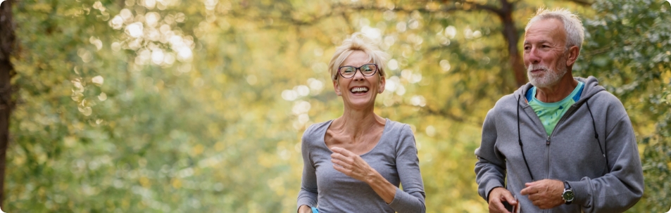 Older man and woman in a park, smiling as they run